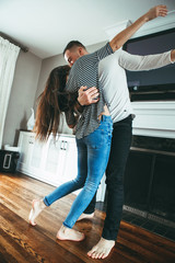 Portrait of beautiful romantic young smiling laughing couple man woman in love hugging, kissing, dancing together indoors at home  in room, toned with filters, authentic candid lifestyle