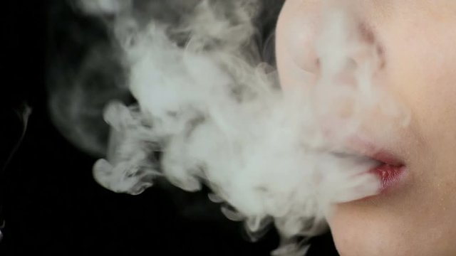 Young Woman Smoking Electronic Cigarette On Black Background. Close-Up