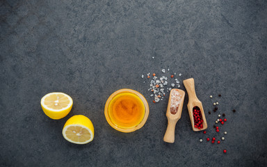 The lemon vinaigrette dressing ingredients lemon, olive oil, himalayan salt and pepper corn on dark stone background with flat lay and copy space.