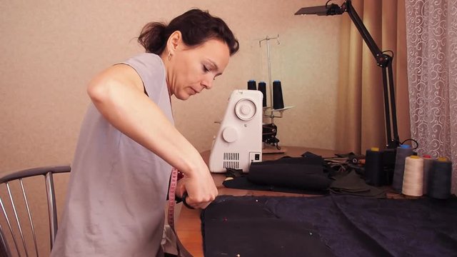 Dressmaker cuts out fabric. Girl cuts fabric with scissors. Stabs pins in the fabric. A woman in a gray T-shirt.