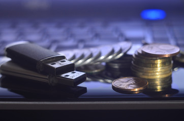 USB memory cards and a few coins lying on the body of black laptop in front of his keyboard....