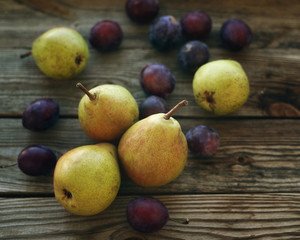 Ripe fresh pears and plums in a bowl on a wooden background close up. Autumn harvest of fruit.