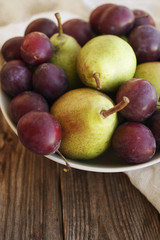 Ripe fresh pears and plums in a bowl on a wooden background close up. Autumn harvest of fruit.