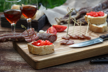 Bread, sausage, red wine, glass, cutting board and knife arranged on a wooden table for a snack in the countryside.