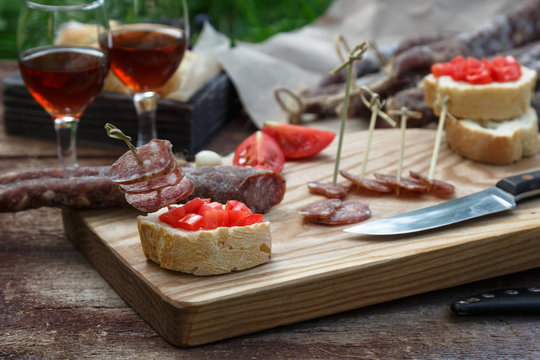 Bread, sausage, red wine, glass, cutting board and knife arranged on a wooden table for a snack in the countryside.