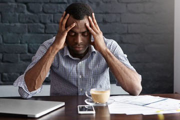 Frustrated young African-American businessman having bad headache, squeezing his temples, feeling...