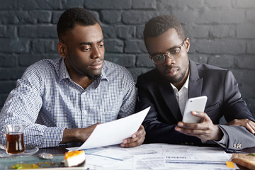 Candida shot of two confident and serious African-American businessmen focused on paperwork,...