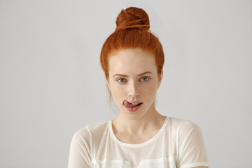 Headshot of attractive tempting woman wearing ginger hair in knot, touching, licking her lips,...