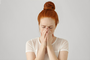 Portrait of unhappy and depressed young Caucasian woman with ginger hair feeling ashamed or sick,...