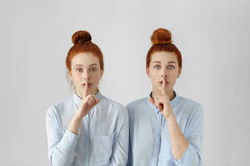 Two beautiful redhead women with same hair buns, dressed in identical formal shirts, keeping...