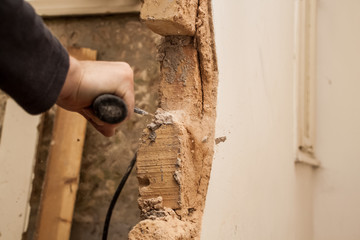 Flat renovation, master mason with a hammer, with a pointy tip of trying to break a brick out of the wall to bring down the wall