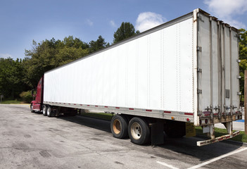 Rear and side view of parked white semi trailer with red cab.