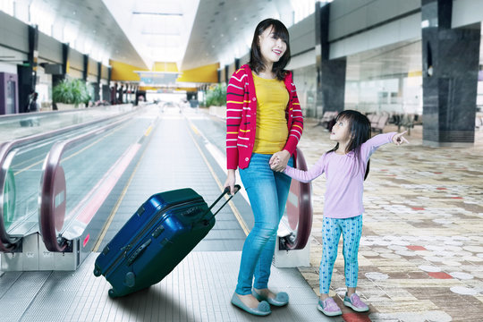 Mother and daughter carrying suitcase at airport