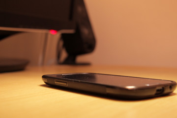 Smartphone placed on wooden table near computer monitor and speakers in orange light toned