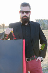 handsome man with a beard in a suit shows shopping bags with space for text, high key