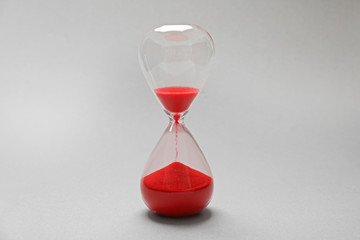 Hourglass with red sand on light background