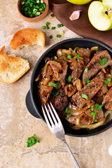 Fried liver with onions and apples on a concrete background