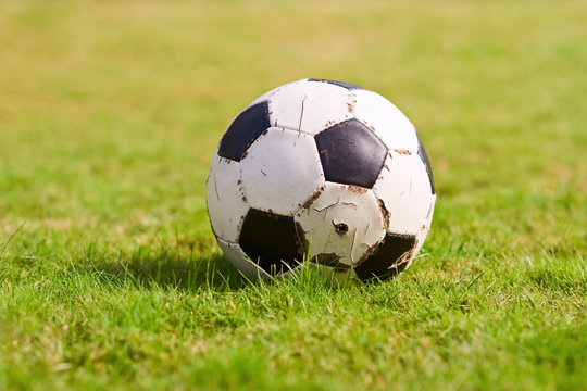 Old soccer ball on green grass. Football on sports field. Sporting goods. Sunny day. Closeup