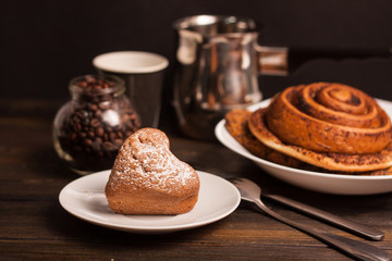 a cake sprinkled with powdered sugar, a cinnamon roll, a bucket and a jar with coffee beans