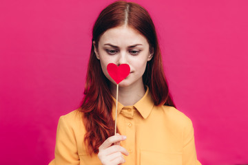 red paper heart on wooden stick in front of woman's lips