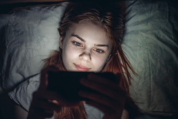 happy woman lies in bed and looks into phone