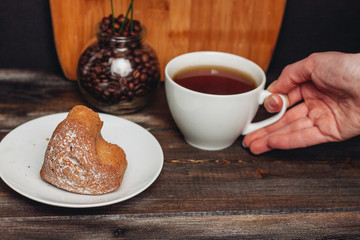 a cup of tea in a hand and a cupcake in a plate, a jar with coffee beans