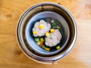 Steamed dimsum or dumpling in a bamboo basket. Minced pork and shrimp wrapped by seaweed topped with pea, corn, carrot. Top view.
