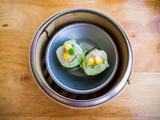 Steamed dimsum or dumpling in a bamboo basket. Minced pork and shrimp wrapped by cabbage leaf topped with pea, corn. Top view.