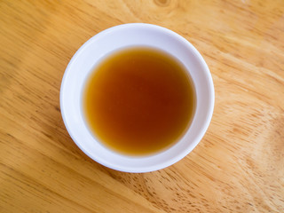 Chinese black vinegar sauce or sour sauce in a small white sauce cup on a wood table background. Dipping sauce for dimsum or dumpling or chinese food.