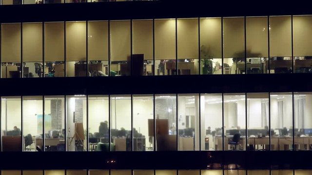 Office building with people working within. Business center with lighting windows with people working overtime. Zoom out effect from the bottom point. Time lapse