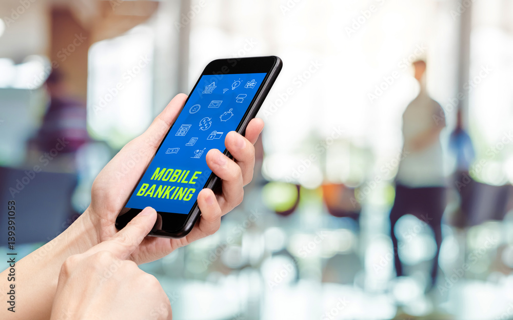 Poster hand holding mobile with mobile banking word and features icon with blur office counter background,d