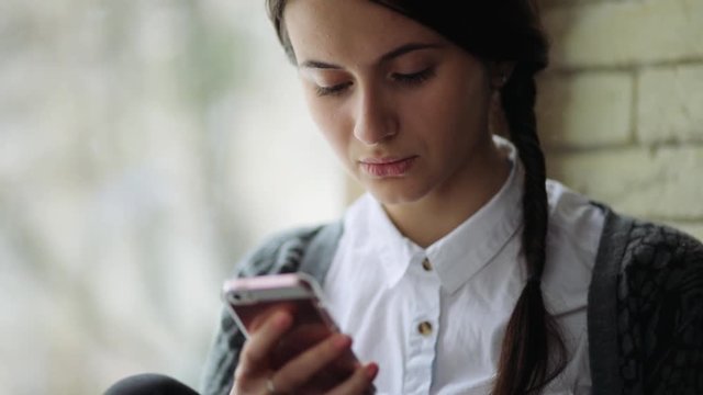 Attractive business woman using mobile phone in the light office near the window feeling sad and miserable.