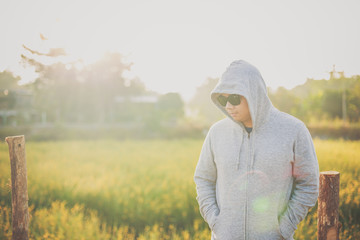 A man wearing a jacket with hood and standing  in a meadow with sunlight in the morning. Winter season concept.