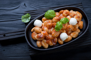 Cast-iron frying pan with potato gnocchi alla Sorrentina on a black wooden background
