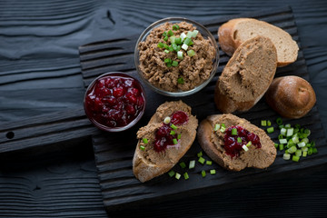 Chicken liver pate with sliced baguette, cranberry sauce and green onion on a black wooden serving board