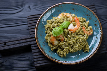 Turquoise plate with spinach and tiger shrimps risotto on a black wooden background, studio shot