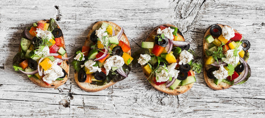 Greek salad style bruschetta on a wooden rustic board, top view. Delicious appetizers for wine or a snack - obrazy, fototapety, plakaty