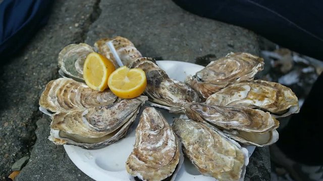 Man sitting on the bank opens an oyster and waters it with lemon juice