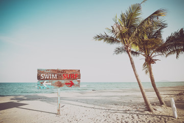 Old wood sign navigate swimming and surfing on a tropical beach in the summer. Vintage color filter effects.
