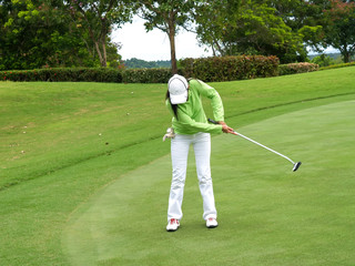 Fototapeta premium Smiling woman golf player putting successfully ball on green, ball dropping into cup,