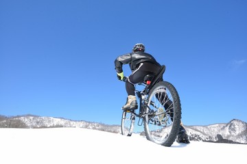 青空の雪原をマウンテンバイクで走る