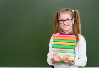 Girl with a pile books near empty green chalkboard