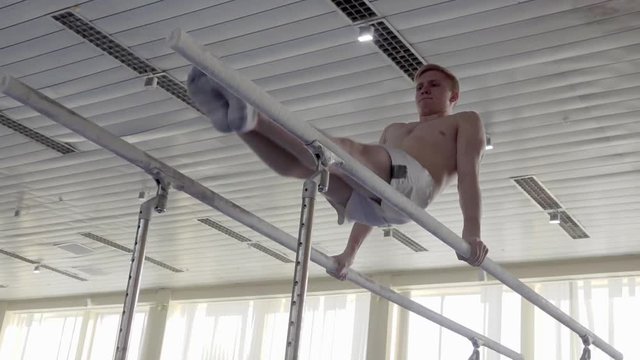 Gymnast performs routine on parallel bars HD gymnastics slow-motion video. Olympics athlete training skills and doing swings acrobatic exercises: hand support, somersault, flip