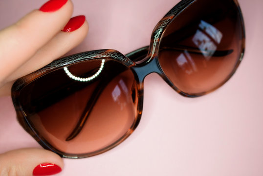 sunglasses in the hand with red nails on pink nackground