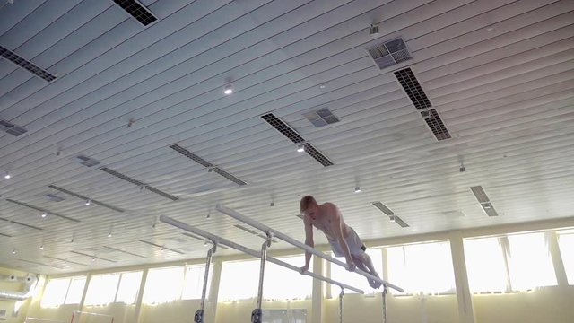 Gymnast performs routine on parallel bars HD gymnastics slow-motion video. Olympics athlete training skills and doing swings acrobatic exercises: hand support, somersault, flip