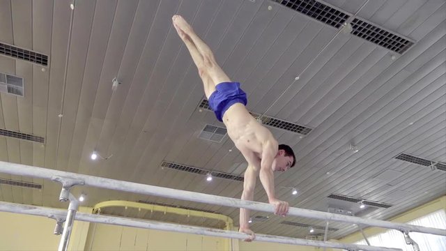 Gymnast performs routine on parallel bars HD gymnastics slow-motion video. Olympics athlete training skills and doing swings acrobatic exercises: hand support, somersault, flip