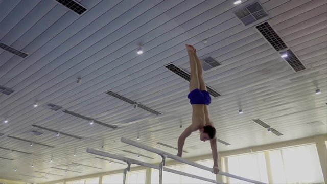Gymnast performs routine on parallel bars HD gymnastics slow-motion video. Olympics athlete training skills and doing swings acrobatic exercises: hand support, flip, handstand