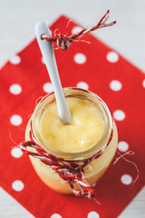 Lemon curd in glass jar with fresh lemons on wooden background