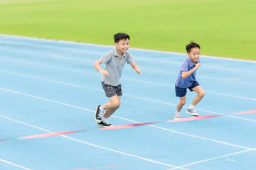 Obraz premium Young Asian boy running on blue track in the stadium