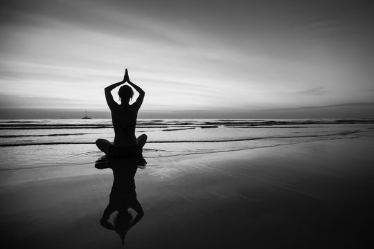 Woman doing meditation near the ocean beach. Black and white silhouette.